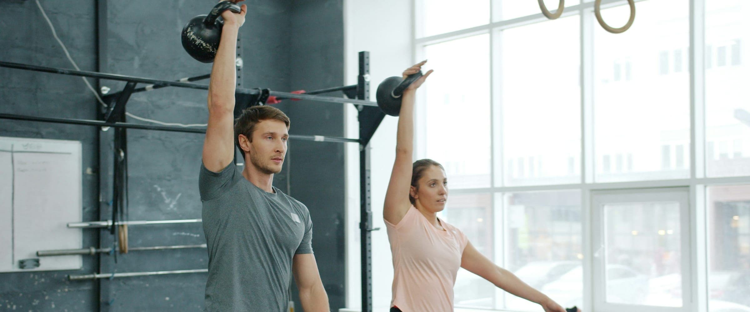 Homem e mulher fazendo balanço de kettlebell lado a lado em um box de treino
